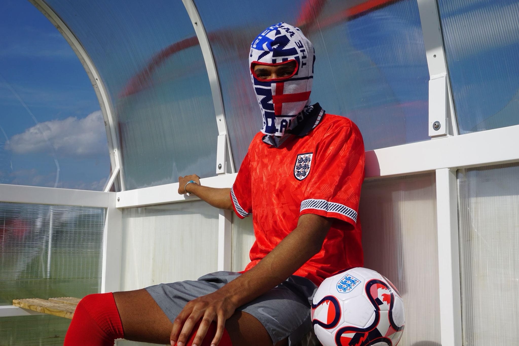 Our model wearing our England football scarf balaclava sitting on a bench with a football